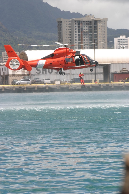 A U.S. Coast Guard helicopter lowers a rescue safety diver into the waters off Honolulu to simulate a life rescue of a dummy. The HH-65 Dolphin hovers overhead as the diver jumps in to save a victim in distress, Sep.1.