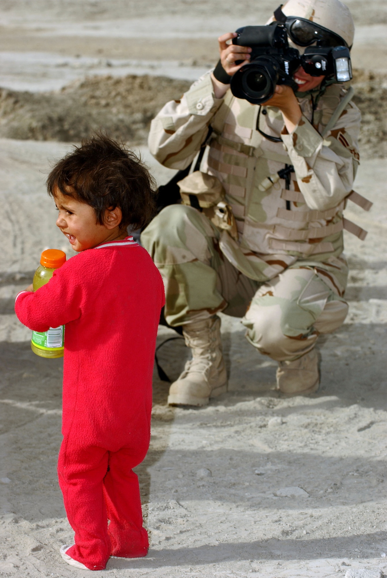 IRAQ -- Airman 1st Class Jamie Shultz photographs a local child outside Ali Base on a security forces mission to interact with locals and provide them a point of contact to call if they see suspicious activity in the area.  Touting an M-16 rifle and 30 pounds of camera equipment, the photographers often leave the safety of the installation's perimeter to document missions affecting Airmen.  Airman Shultz is a photographer with the 407th Expeditionary Communications Squadron base multimedia center.  (U.S. Air Force photo by Master Sgt. Maurice Hessel)