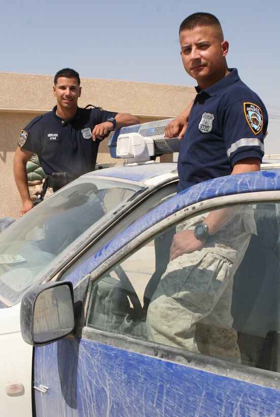Staff Sgt. Jose Mercado (rear) and Sgt. Nelson Vergara, both with Mobile Training Team, Iraqi Security Force, II Marine Expeditionary Force (FWD), stand in front of a police car at the ISF compound on Camp Fallujah. Both reserve Marines, who attached to II MEF (FWD) from 2nd Battalion, 25th Marines, 4th Marine Division, based in Garden City, N.Y., were on the scene as the events of 9/11 unfolded, serving as New York City police officers.