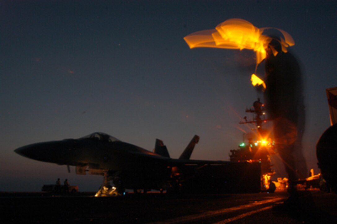 A U.S. Navy Aviation Boatswain Mate signals to an F/A-18E Super Hornet assigned to Strike Fighter Squadron 143 that they are clear for launch during night flight operations aboard the aircraft carrier USS John F. Kennedy (CV 67) underway in the Atlantic Ocean on Sept. 19, 2005. 