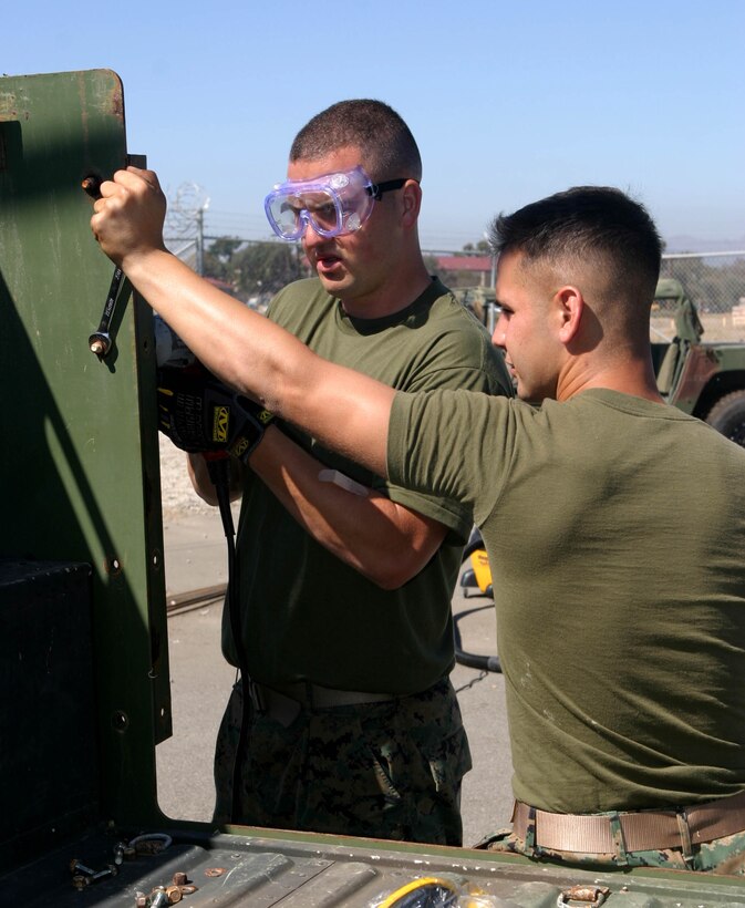 Cpl. Gilbert J. Unger, left, an operations and training non-commissioned officer with the 15th Marine Expeditionary Unit, and a native of Neptune, N.J., and Lance Cpl. Carlos M. Forero, a field radio operator, and native of Orlando, Fla., remove a class 2 armored door from a humvee in their motor pool at Camp Del Mar here. The 15th MEU removed their class 2 armor in preparation for installing MAK 1 armor.