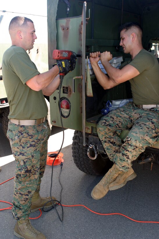 Cpl. Gilbert J. Unger, left, an operations and training non-commissioned officer with the 15th Marine Expeditionary Unit, and a native of Neptune, N.J., and Lance Cpl. Carlos M. Forero, a field radio operator, and native of Orlando, Fla., remove a class 2 armored door from a humvee in their motor pool at Camp Del Mar here. The 15th MEU removed their class 2 armor in preparation for installing MAK 1 armor.