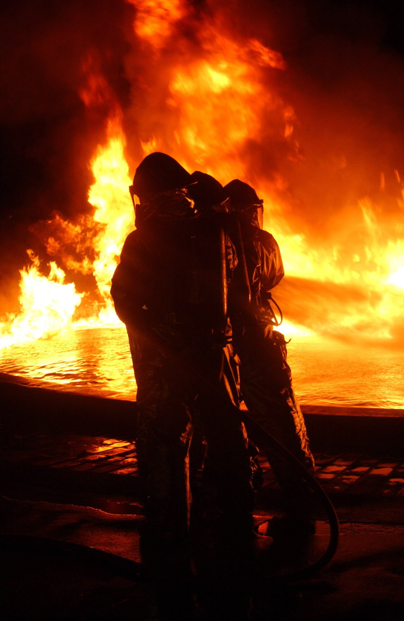 MARINE CORPS AIR STATION FUTENMA, Japan -- Kadena fire emergency services Airmen fight a blaze in a live fuel fire pit here Sept. 22.  Their suits can withstand radiant temperatures of up to 2,000 degrees.  The 18th Civil Engineer Squadron Airmen used the Marine facility for training while theirs is undergoing maintenance.  (U.S. Marine Corps photo by Pfc. Terence L. Yancey)