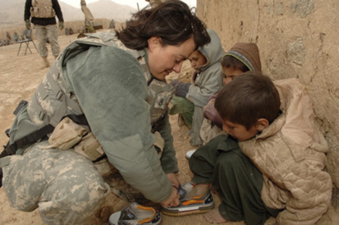 Staff Sgt. Elena Varela, U.S. Army, helps a local Afghan child lace his new pair of donated shoes during a village medical outreach at Khakeran Village, Qalat province, Afghanistan, on March 18, 2006. 