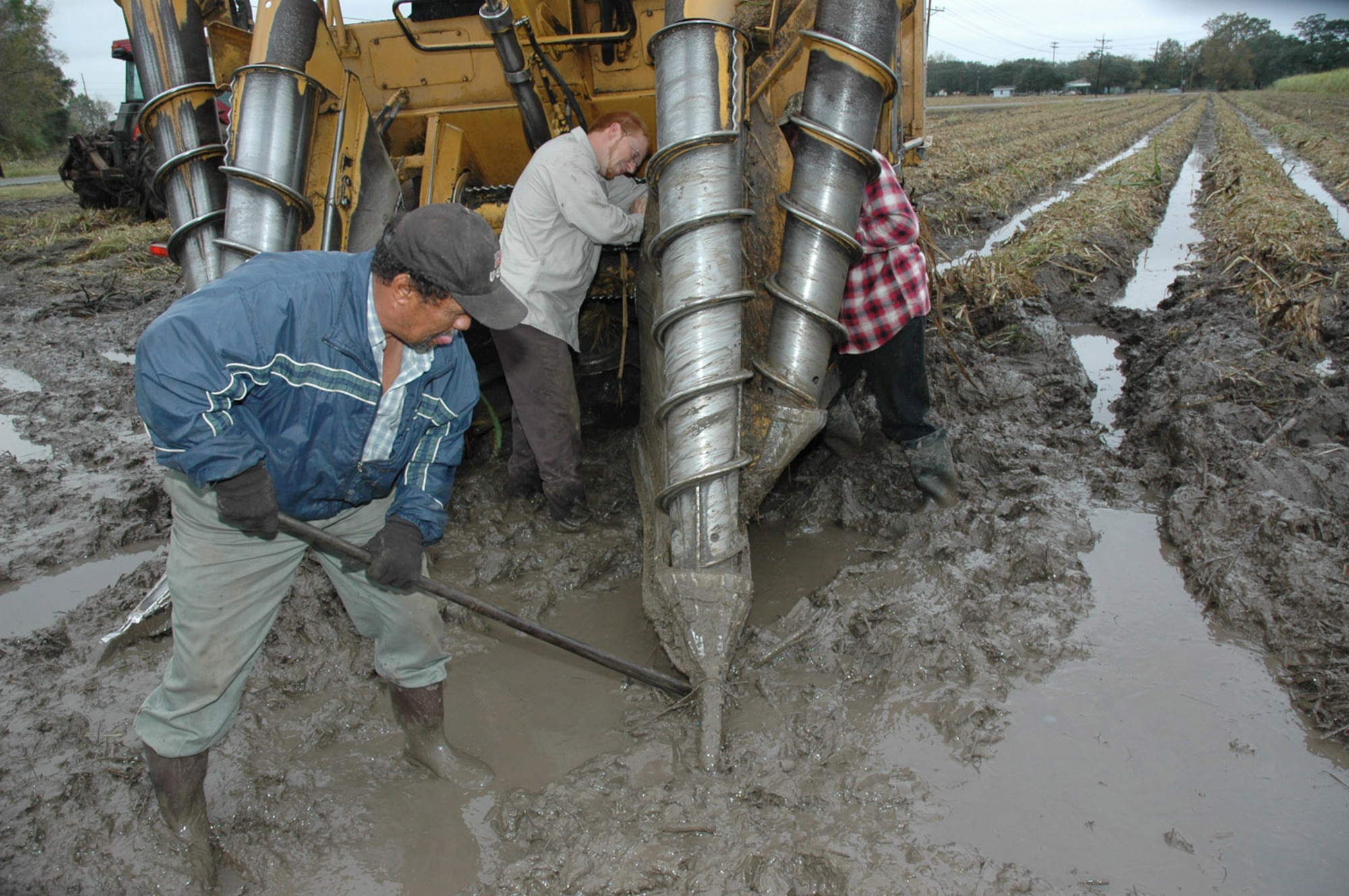 Staff Sgt. Kent Roberts and two workers struggle in the mud to repalce a screw that broke from the combine during harvesting. The muddy conditions are part of the business in south Louisiana. As soon as the part is replaced, Sergeant Roberts gets back in the combine and continues harvesting. He is a reservist with the 926th Fighter Wings at Naval Air Station Joint Reserve Base New Orleans.  (U.S. Air Force photo/Master Sgt. Chance Babin)