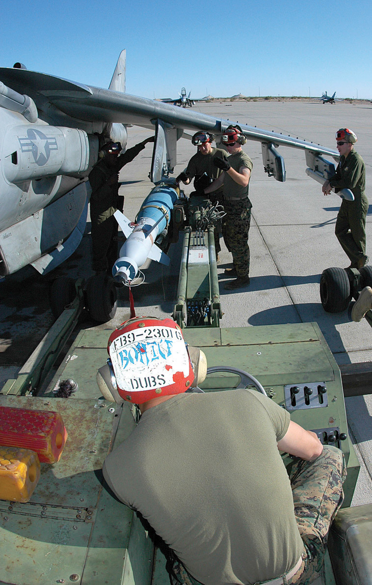 Cpl. Joey Ellis, Marine Attack Squadron 231 aviation ordnanceman, carefully drives an inert version of a Guided Bomb Unit 16 (GBU-16) -- a MK-83 1,000-pound bomb modified with a Paveway II laser guidance kit -- into position under a VMA-223 AV-8B Harrier at the Combat Arms Loading Area here April 6. Other VMA-231 Marines wait under the wing to direct and quickly attach the bomb to one of the jet?s loading stations using Preload Accessory Suspension Equipment. PASE loading allows ordnancemen to rapidly re-arm jets while their engines are turning, which saves precious time in theater. Under the direction of MAWTS-1, 11 Marines received training on PASE loading during Weapons and Tactics Instructor Course 2-06.