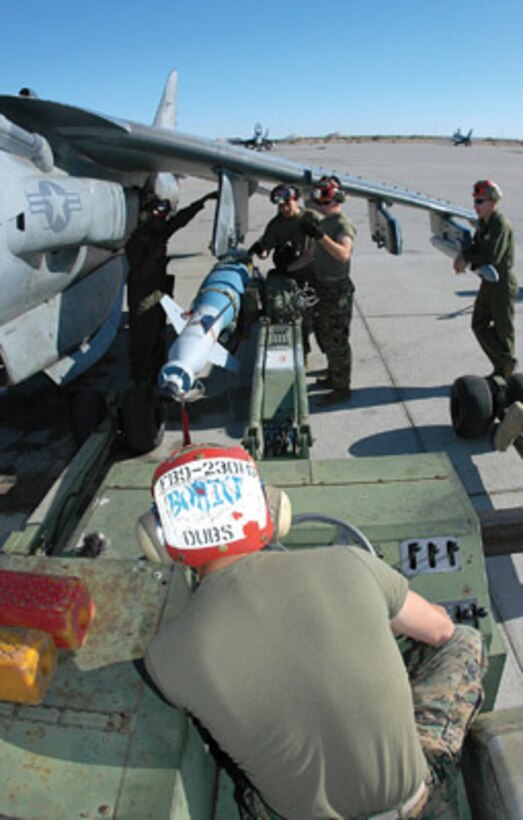 Cpl. Joey Ellis, Marine Attack Squadron 231 aviation ordnanceman, carefully drives an inert version of a Guided Bomb Unit 16 (GBU-16) -- a MK-83 1,000-pound bomb modified with a Paveway II laser guidance kit -- into position under a VMA-223 AV-8B Harrier at the Combat Arms Loading Area here April 6. Other VMA-231 Marines wait under the wing to direct and quickly attach the bomb to one of the jet?s loading stations using Preload Accessory Suspension Equipment. PASE loading allows ordnancemen to rapidly re-arm jets while their engines are turning, which saves precious time in theater. Under the direction of MAWTS-1, 11 Marines received training on PASE loading during Weapons and Tactics Instructor Course 2-06.