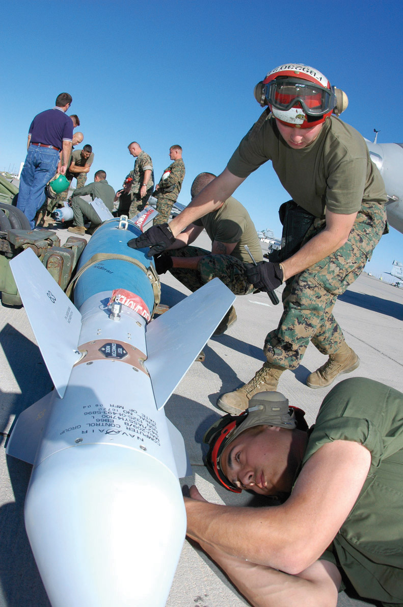 Lance Cpl. Francisco Iniguez, Marine Attack Squadron 211 aviation ordnanceman, and Lance Cpl. Michael Bennett, VMA-231 ordnanceman, attach fins to the nose of a Guided Bomb Unit 16 (GBU-16) -- a MK-83 1,000-pound bomb modified with a Paveway II laser guidance kit -- at the Combat Arms Loading Area here April 6.
