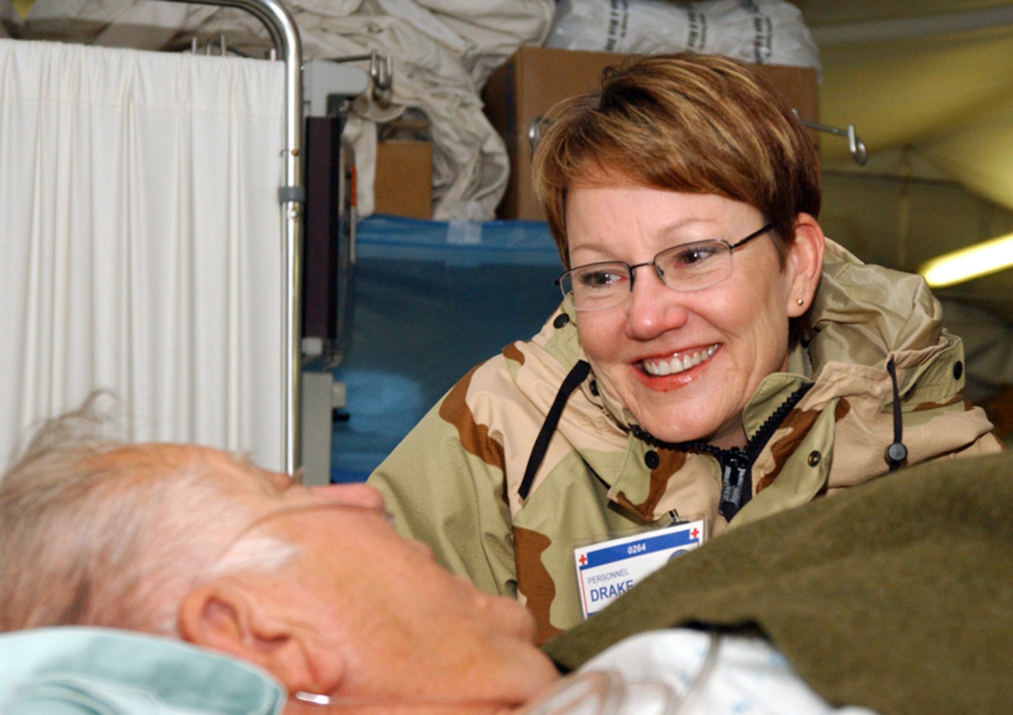 Lt. Col. Beth Drake keeps company with Sam Lee on Tuesday, April 4, 2006, at the Air Force Theater Hospital at Balad Air Base, Iraq, while he waits to be moved to an aircraft. Colonel Drake is associate chief nurse of the Contingency Aeromedical Staging Facility; Mr. Lee is a labor foreman from a forward operating base (U.S. Air Force photo/Staff Sgt. Robert Wollenberg) 
                         
