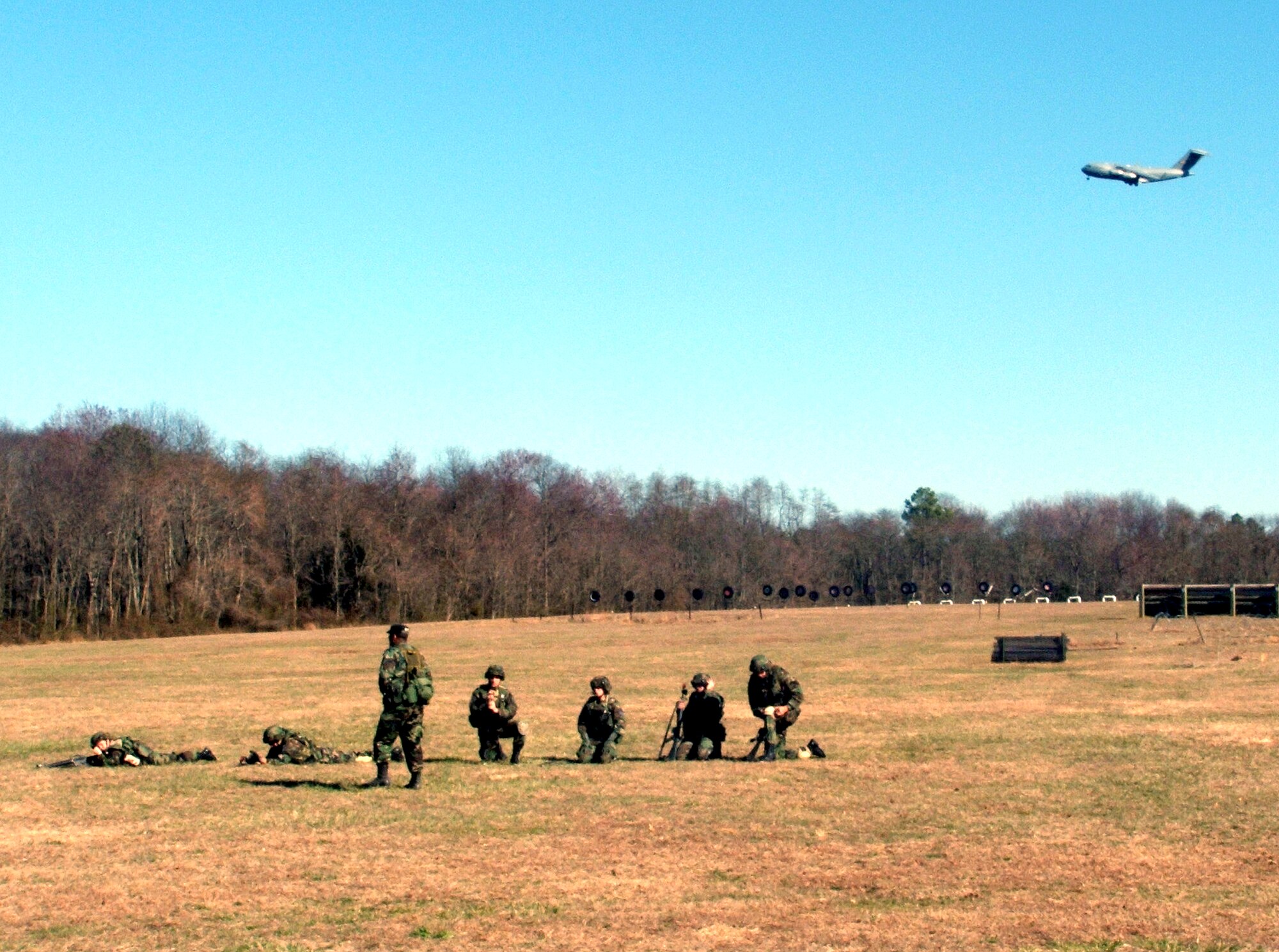 Airmen practice combat tactics and squad patrolling maneuvers on Monday, March 27, 2006, during the Air Force Integrated Contingency Skills Training Course 06-3 at Fort Dix, N.J.  A Globemaster III from McGuire Air Force Base, N.J., flies overhead. The Air Mobility Warfare Center's 421st Combat Training Squadron instructors trained more than 140 Airmen in combat tactics and convoy operations to prepare for deployments for the Air Force. (U.S. Air Force photo/Tech. Sgt. Scott T. Sturkol) 
