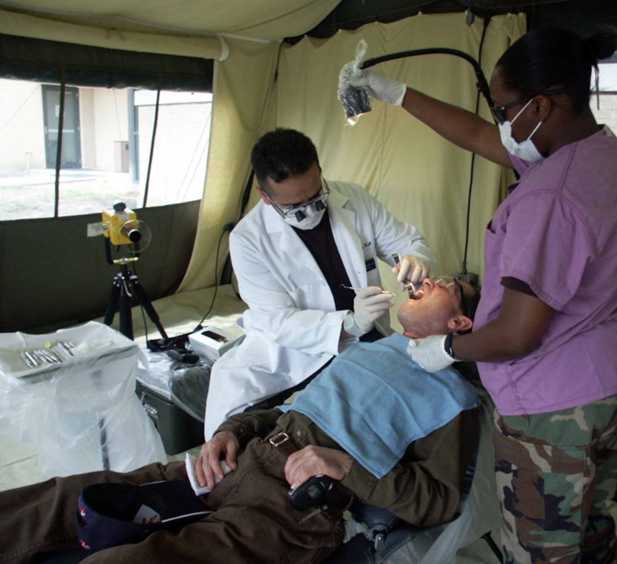 Periodontal resident Maj. (Dr.) Jesse Murillo works on Robustino Rodriguez with dental assistant Staff Sgt. Letrice Mitchell on Thursday, April 6, 2006. The patient, a retired Army staff sergeant, volunteered to take part in the expeditionary field dental training at Lackland Air Force Base, Texas, April 3 through 7. (U.S. Air Force photo/Master Sgt. Kimberly Spencer)
