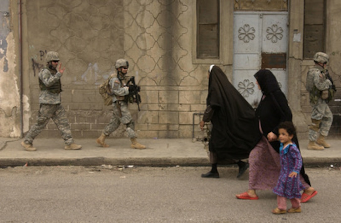 U.S. Army soldiers wave and smile as they pass by two Iraqi women and a child during a neighborhood foot patrol in Mosul, Iraq, on April 12, 2006. The soldiers are attached to the 1st Battalion, 17th Infantry Regiment, 172nd Infantry Brigade Combat Team. 