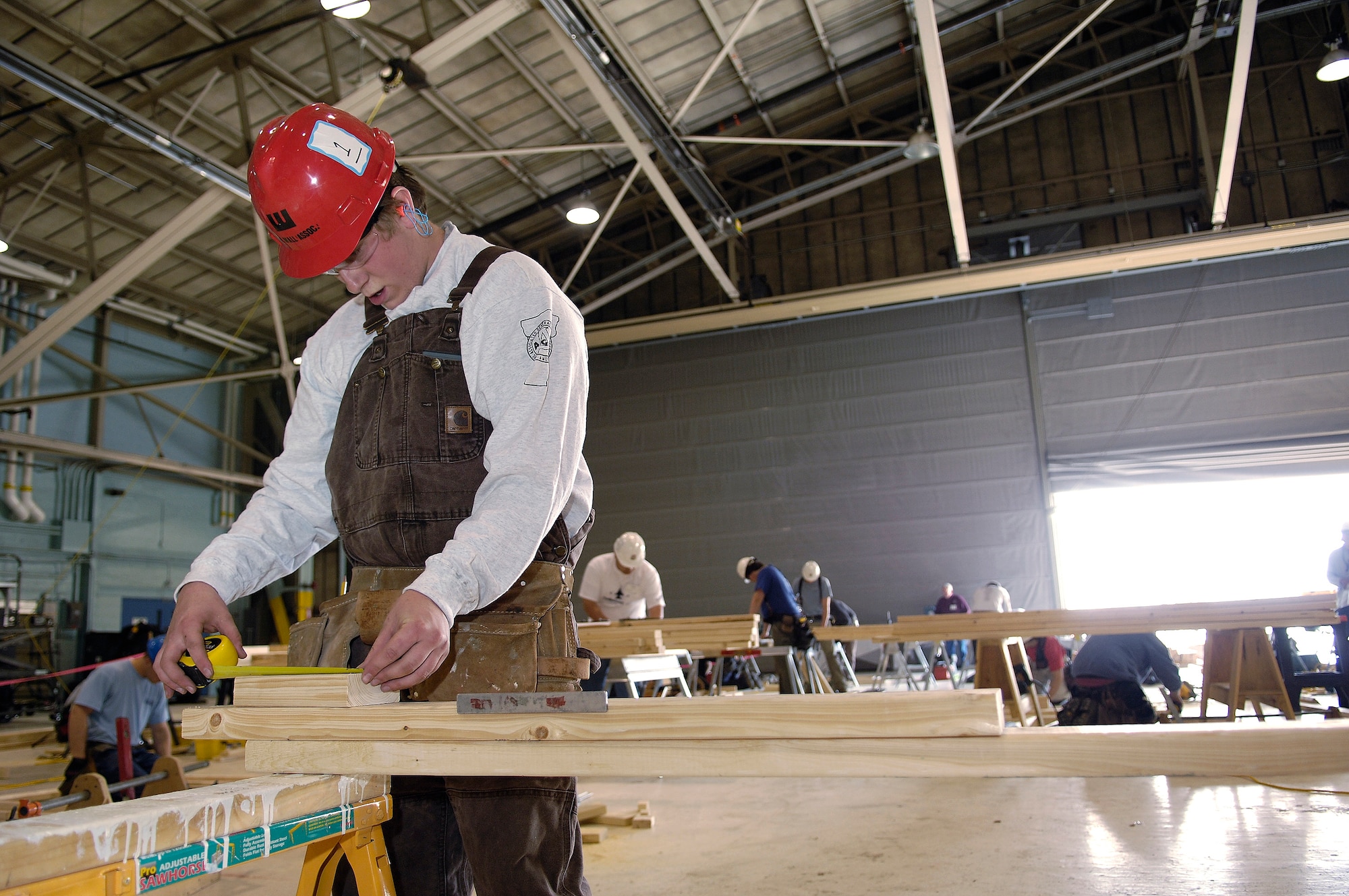 SkillsUSA competitor Travis Bombard measures a two-by-four during carpentry competition at the Vermont Air National Guard base in South Burlington, Vt. The hangar normally serves as a weapons loading bay for the unit's F-16 Fighting Falcons. Mr. Bombard is a 12th grader at Barre Technical Center in Barre, Vt. (U.S. Air Force photo by Master Sgt. Rob Trubia)