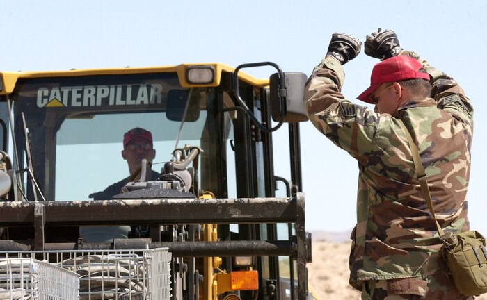 Tech. Sgt. Jeremy Hamilton receives marshaling instructions from Staff Sgt. Jeff Ray during a bare-base build-up exercise at Nellis Air Force Base, Nev., April 8 to 9, 2006. The operation consisted of beddown and construction operations for 120 Airmen. The camp had a mobile field kitchen with generators, reverse-osmosis water purification unit and field latrine equipment. Both Airmen are with the 555th Red Horse Civil Engineer Squadron. (U.S. Air Force photo/Master Sgt. Kevin J. Gruenwald)