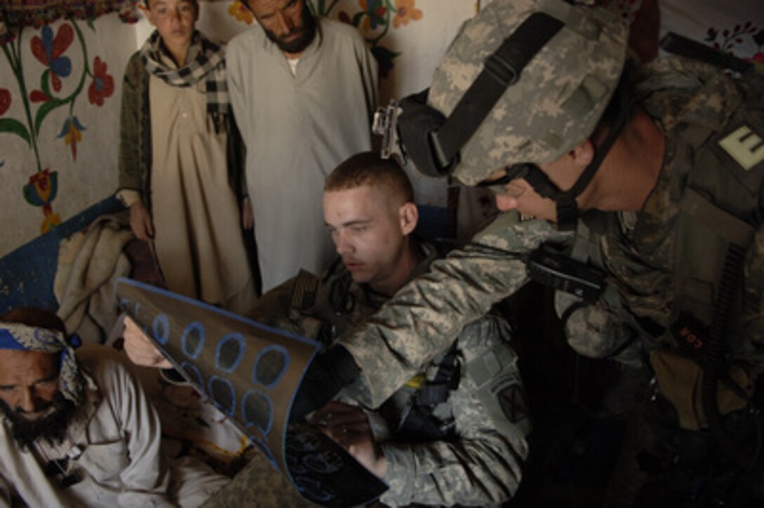 Curious villagers watch as Army Capt. Jason Toole (right) and Spc. Nick Cannole evaluate the results of a CAT scan of a man who suffered a stroke in Makawa, Afghanistan, on April 15, 2006. Tool, the commander of Alpha Company and Cannole, a medic from Alpha Company, are assigned to the 3rd Brigade Special Troops Battalion, 10th Mountain Division. 