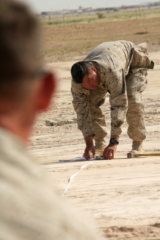 Staff Sgt. Rex Coste glances up at Cpl. Travis G. Hill while measuring the distance from the newly installed marshalling pad to the location of a future impact site, giving aircraft a safe place to arm and disarm their weapons at Al Asad, Iraq, April 21. Coste is a runway supervisor with Marine Wing Support Squadron 274, Marine Wing Support Group 37 (Reinforced), 3rd Marine Aircraft Wing, and Hill is a heavy equipment operator with the engineering company of MWSS-274. Coste is a native of San Antonio, and Hill is a Mesa, Ariz., native.