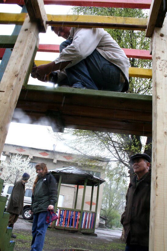 A groundskeeper watches Senior Airman John Burgess put final touches on monkey bars he designed for the playground outside the Belovodsky Orphanage for children with special needs. Airman Burgess has volunteered many off-duty hours helping design and build playground equipment for the orphange, located in Belovodsky, Kyrgyzstan. (U.S. Air Force photo/Staff Sgt. Lara Gale)