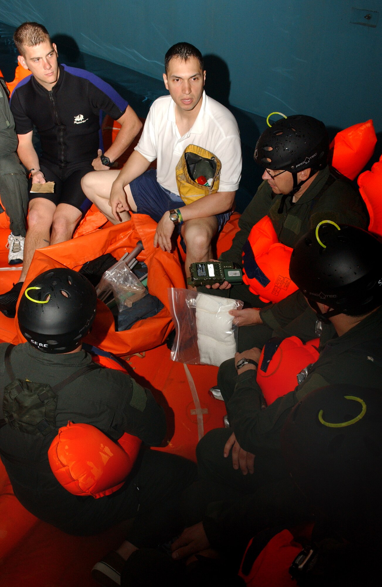 Tech Sgt. Rob Graham, top center, a 100th Operations Support Squadron survival, evasion, resistance and escape specialist, and Senior Airman Derek Owens, top left, 352nd Special Operations Group SERE specialist, show students the contents of a 20-man life raft survival kit and explain for what each item in the can be used June 8 during water-survival training in Lowestoft.  (U.S. Air Force photo by Staff Sgt. Tyrona Pearsall)