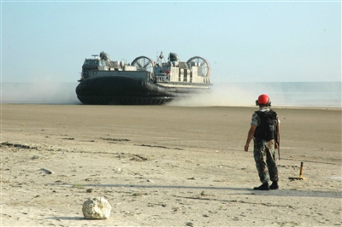 A U.S. Navy sailor keeps the beach clear as a Navy Landing Craft Air Cushion, more commonly known as an LCAC, from Assault Craft Unit 5 comes ashore at Mersing, Malaysia, on July 30, 2006.  The LCAC and her crew are taking part in the fourth phase of Cooperation Afloat Readiness and Training, an annual series of bilateral maritime training exercises between the United States and six Southeast Asian nations.  