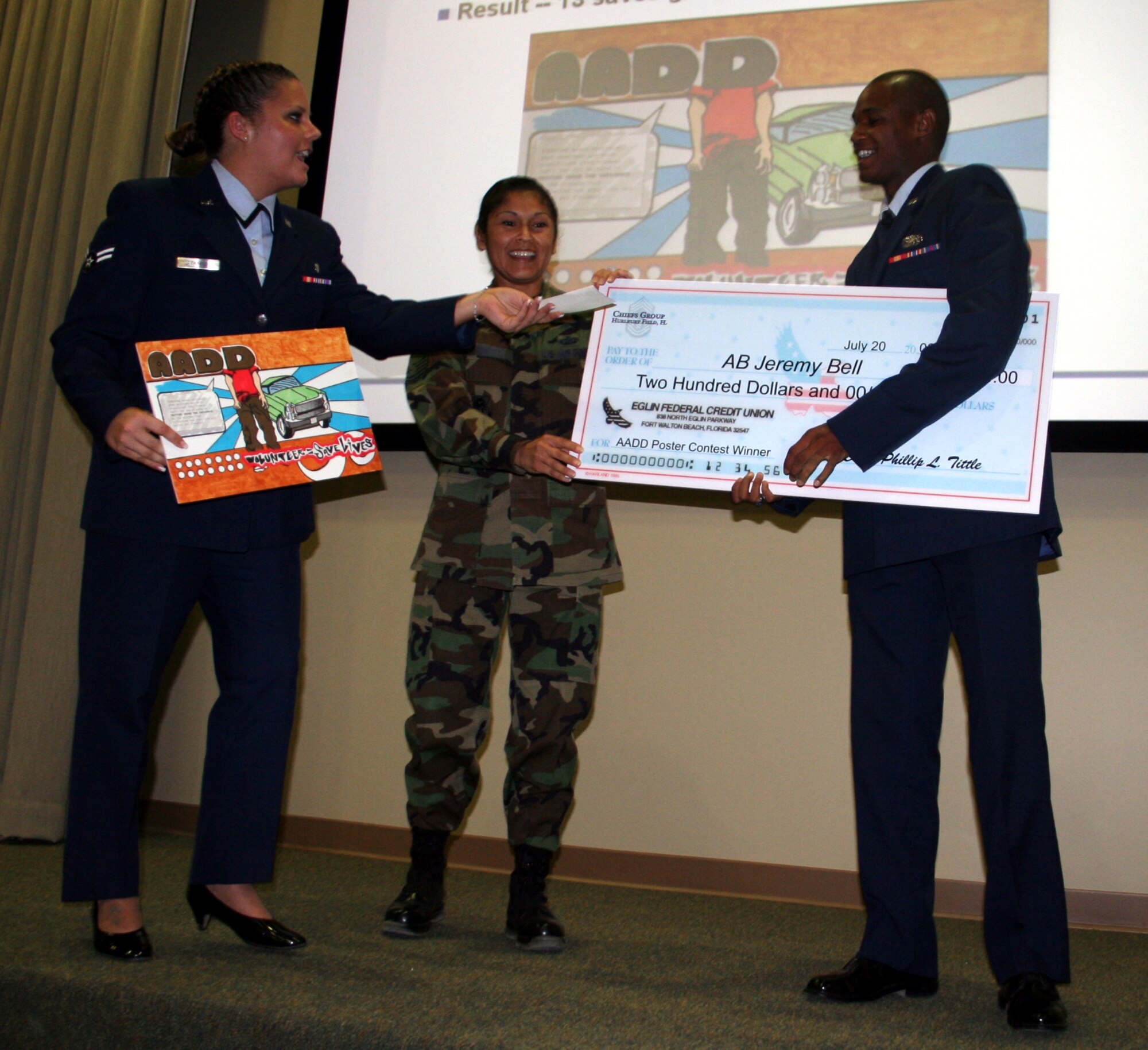 Airmen Against Drunk Driving Treasurer (left) Airman 1st Class Megan Stanton, 16th Medical Support Squadron, and AADD President Master Sgt. Myra Casanova, 16th Mission Support Squadron, hand Airman Basic Jeremy Bell, 505th Training Squadron, a check for $200 for his award-winning AADD poster. (U.S. Air Force Photograph by Jamie Haig) 
