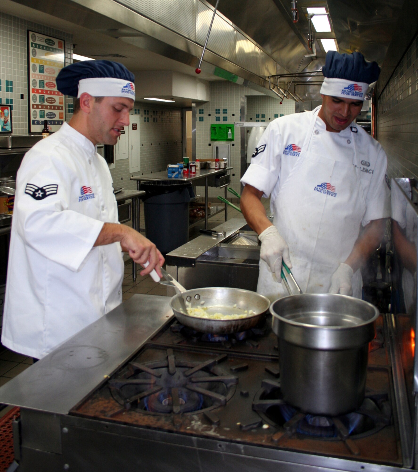 Senior Airman James Vest (left) and Airman 1st Class Louis Velencia, both with 16th Services Squadron, share a stove during the Chef of the Quarter cook-off competition held July 21 in The Reef dining facility. (U.S. Air Force Photograph by Jamie Haig)