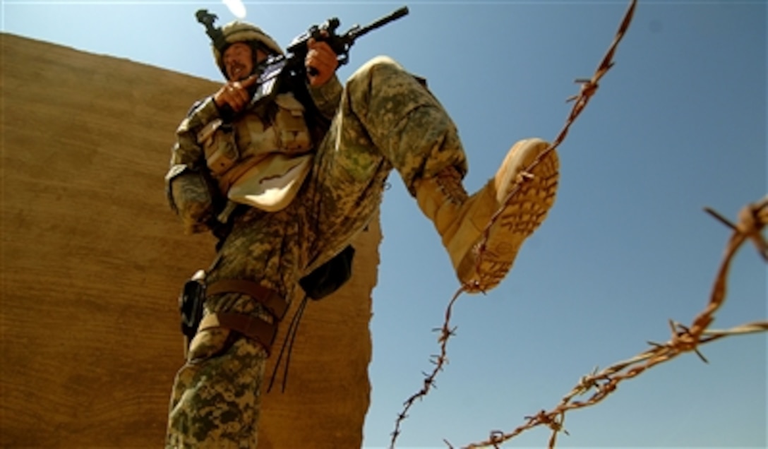 A U.S. Army soldier steps over strands of barbed wire as he searches for insurgents across the street from Outpost 293 in Ramadi, Iraq, on July 24, 2006.  Soldiers from the 1st Armored Division began the search after a mortar attack and gunfire were received on the outpost.  