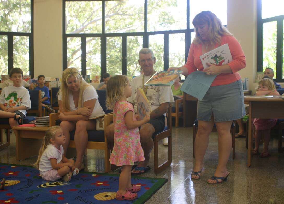 Summer Reading Program coordinator Merri Fernandez hands  a prize to Brittany Anderson, 2, during the Summer Reading Program Wrap Up Party at the Base Library here Saturday for completing the most books during the duration of the program in her age category. The program is put on every year as a way to encourage kids to be lifelong readers, according to Fernandez.