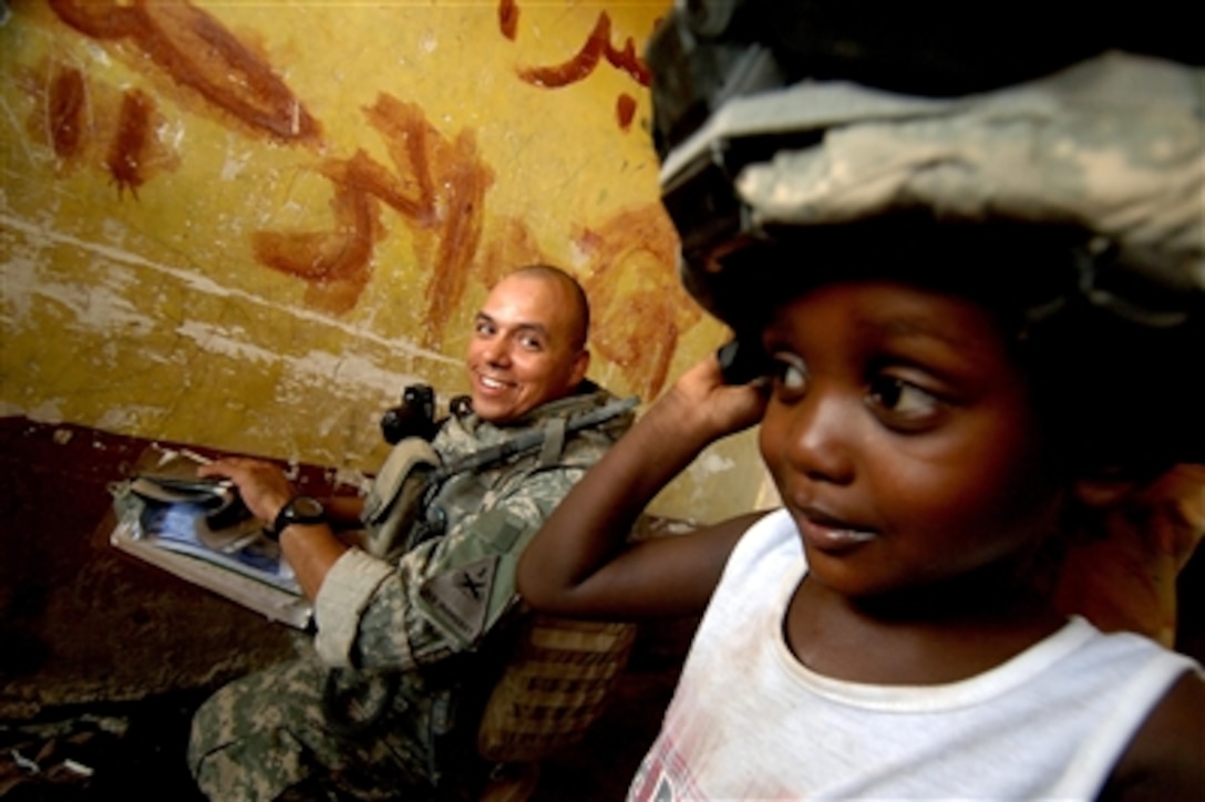 U.S. Army Sgt. Jose Lanzarin watches as a young Iraqi girl tries on his Kevlar helmet while he and his team question her mother in order to fill out a census form in Tameem, Iraq, on Aug. 7, 2006.  The census is being conducted to gather general information about Iraqi households and to see if citizens have any concerns or questions that the soldiers can answer.  Lanzarin is from Bravo Company, 2nd Battalion, 6th Infantry Regiment, attached to Task Force 1st Battalion, 35th Armored Regiment, 2nd Brigade Combat Team, 1st Armored Division.  