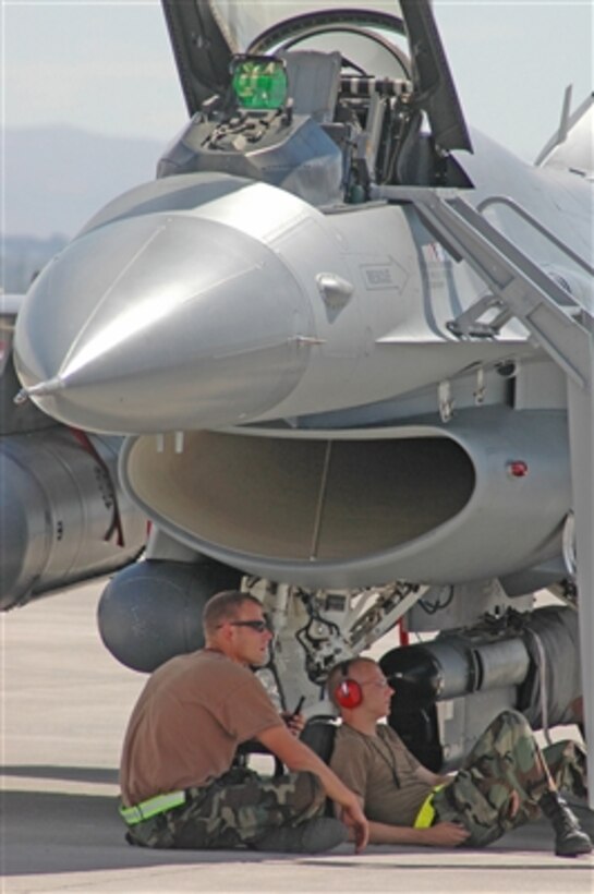 Air Force Senior Airmen Brent Bott (left) and Zack McLaughlin seek shade under an F-16 Fighting Falcon aircraft between launches during exercise Red Flag 06-02 at Nellis Air Force Base in Las Vegas, Nev., on Aug 9, 2006.  Both airmen are attached to the 132nd Fighter Wing, Iowa Air National Guard.  