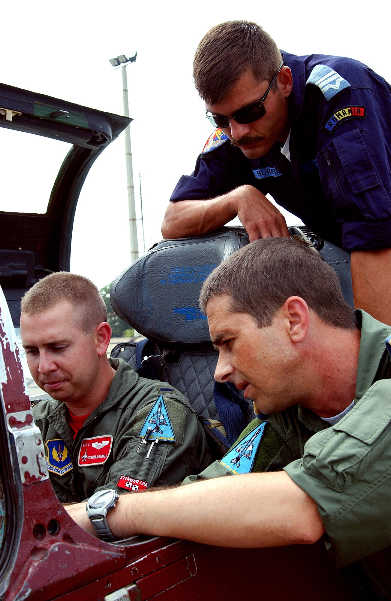 First Lt. Coleman McDonald sits in the cockpit of a MiG-21 Lancer at Mihail Kogalniceanu Air Base, Romania, on Aug. 11, while Lt. Cmdr. Eugene Matache (lower right) and Warrant Officer Third Class Sorin Burdusel of the Romanian air force walk through operating instructions. Lieutenant McDonald is an F-16 Fighting Falcon pilot with the 22nd Expeditionary Fighter Squadron participating in Viper Lance 2006. (U.S. Air Force photo/Senior Airman Eydie Sakura)