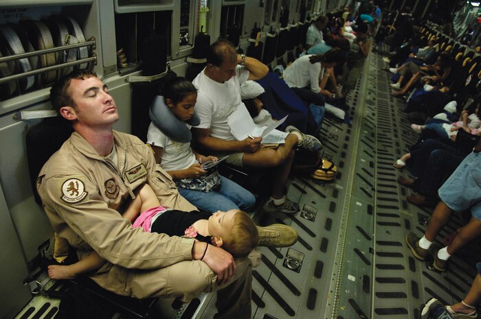 In order to ease the burden of a single-mother American evacuee,  Airman 1st Class Jarod Lambert, 16th Airlift Squadron loadmaster, holds one of the evacuees, as they fly aboard a C-17 headed to Ramstein AB, Germany, July 23. After 99 American evacuees arrived in Cyprus from Lebanon, members of the 16 AS provided them transportation to Germany. This C-17 crew was the first Air Force aircrew to airlift American citizens out of that region. (U.S. Air Force photo by Staff Sgt. Stacy Pearsall)