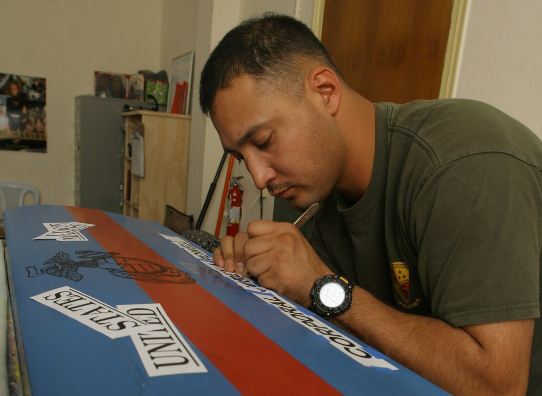 Staff Sgt. John A. Flores cuts out a stencil on a helicopter blade he is converting into plaque for another Marine, Aug. 18, at Al Asad, Iraq. Flores, a career retention specialist with Marine Aviation Logistics Squadron 16, Marine Aircraft Group 16 (Reinforced), 3rd Marine Aircraft Wing (Forward), paints used rear-rotor helicopter blades and transforms them into Marine Corps memorabilia. Flores is a San Antonio native.