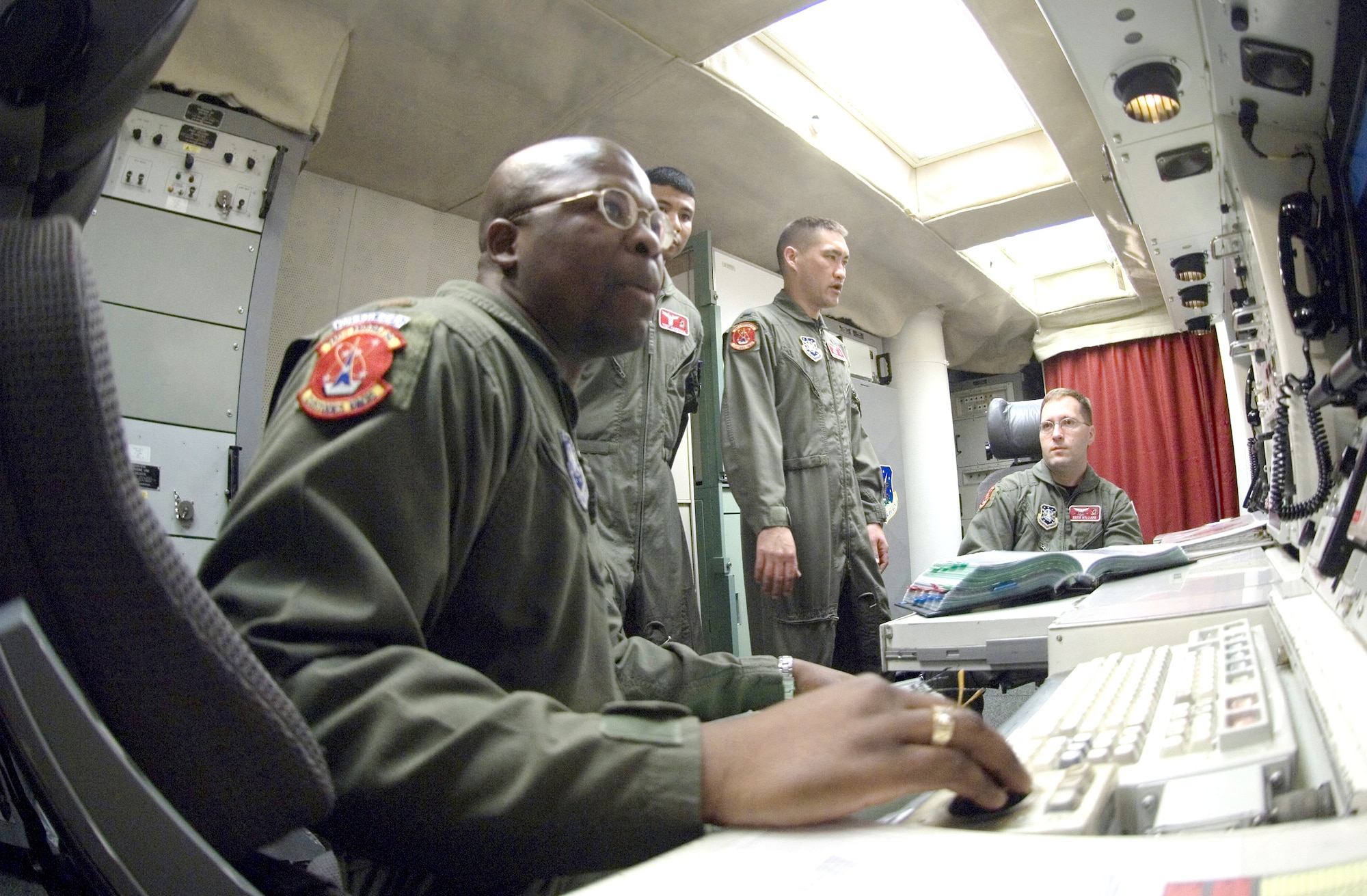 In the underground launch control center at Minot Air Force Base's Missile Alert Facility B-1, one of 15 91st Space Wing MAFs scattered across northwest North Dakota, the on-duty missile combat crew prepares to turn over responsibility for the Minuteman III missiles in their control to the on-coming crew Aug. 18.  Second Lt. Nicholas Smith (seated left) and 1st Lt. Eddie Williams (seated right) brief 1st Lt. John Manibusan (left) and 2nd Lt. Trey Marshall (right) on the status of the MAF, the control center and missiles.  All four crew members are with the 740th Missile Squadron. (U.S. Air Force photo/Master Sgt. Lance Cheung) 
