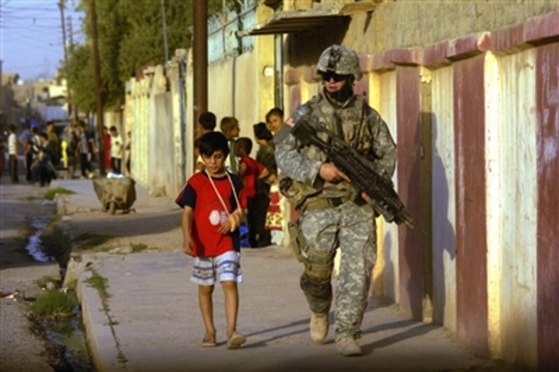 An Iraqi boy walks beside U.S. Army Spc. Andrew Ruhlman as he conducts a presence patrol in Tall Afar, Iraq, on Aug. 13, 2006.  Ruhlman is attached to the 1st Brigade Combat Team, 2nd Battalion, 37th Armored Regiment, 1st Armored Division.  