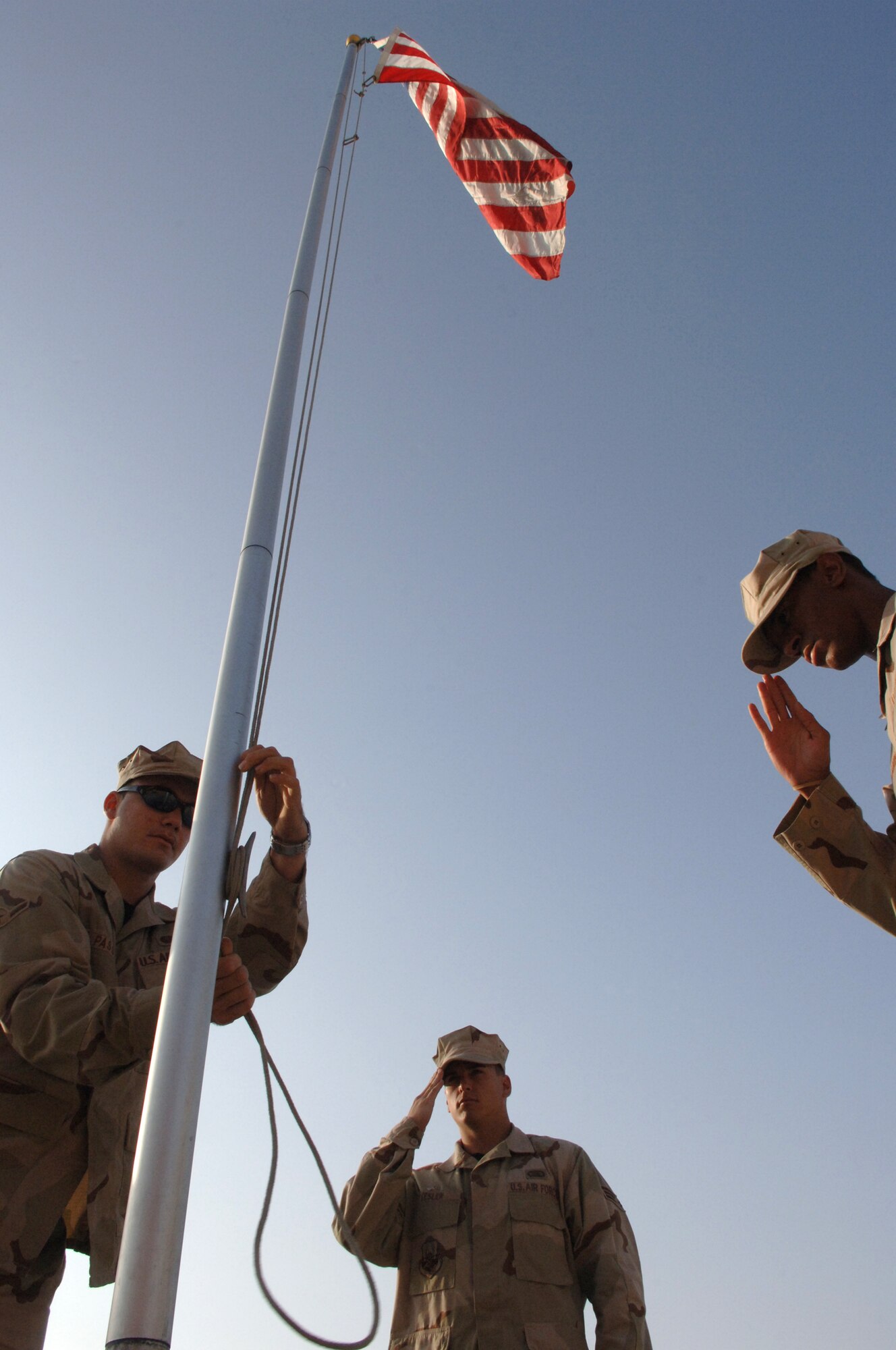 Airman Gordan Passen ties off a lanyard to the Camp Cunningham flag pole while Senior Airman Doug Kesler, center, and Airman 1st Class Santron Benjamin render salutes Aug. 23.  Airman Passen and Kesler are in the 455th Expeditionary Mission Support Squadron and Airman Benjamin is in the 455th Air Expeditionary Wing. They are all deployed to Bagram Airfield, Afghanistan. (U.S. Air Force photo by Master Sgt. Orville F. Desjarlais Jr.)