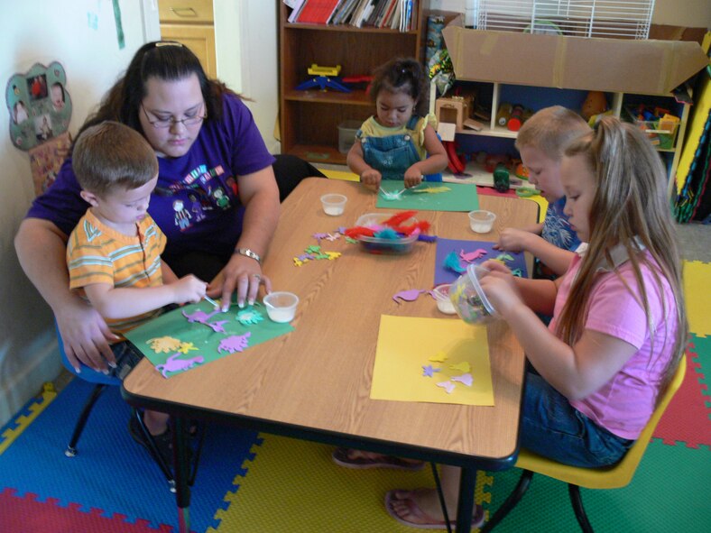 Carla Johnson (second from left), Family Child Care licensed provider, helps Ryan Cook glue a dinosaur to his paper Monday at her home in base housing. Mrs. Johnson has been a certified provider for almost five years.  (U.S. Air Force Photo/Senior Airman S.I. Fielder)