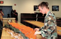 Senior Airman Jacoby Bruner, 388th Equipment Maintenance Squadron survival equipment specialist, inspects a parachute while local camera crews watch on.