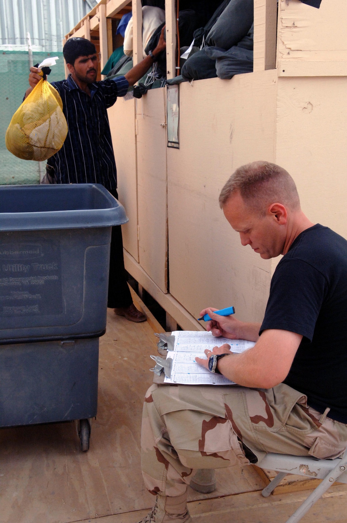 A Kellogg, Brown and Root employee transfers a clean bag of laundry into a bin while Tech. Sgt. Aaron Norfleet checks the inventory list a final time before delivering it to Camp Cunningham. It takes 85 local Afghans working 24-hours a day to handle Bagram's laundry load. (U.S. Air Force photo by Master Sgt. Orville F. Desjarlais Jr.) 