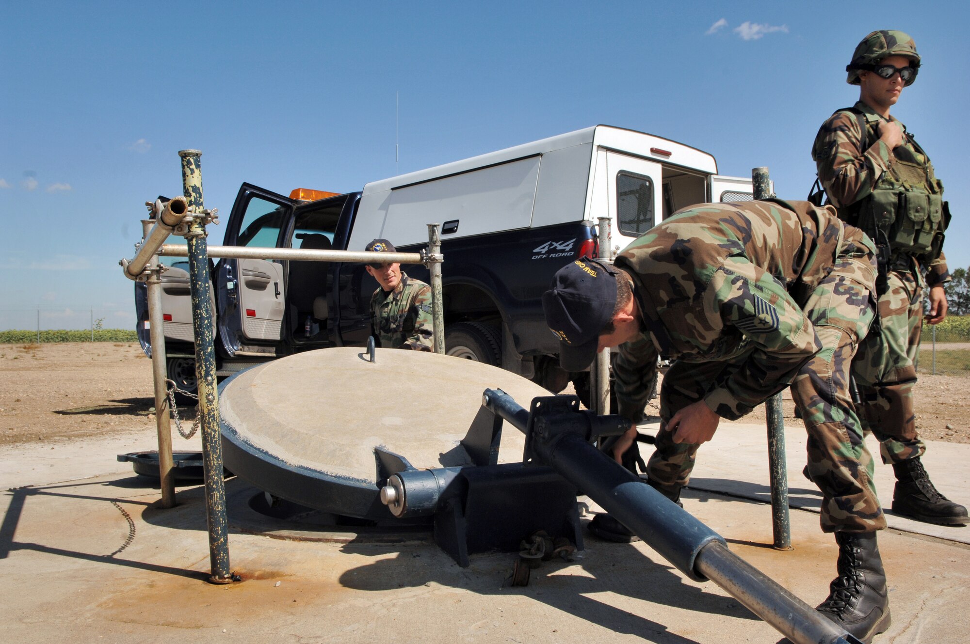 Tech. Sgt. Adam Chandler (center) lowers a reinforced cement protective lid to the personnel access tube while Airman 1st Class Christopher Ramirez (right) keeps an eye on security at a Minuteman III intercontinental ballistic missile launch facility Aug. 25. Security is accomplished with a multi-ton plug that seals the passageway and uses vault-style steel pins to lock it into place. The Airmen are missile handling and security team members with the 91st Missile Wing at Minot Air Force Base, N.D. (U.S. Air Force photo/Airman 1st Class Chris Boitz)
