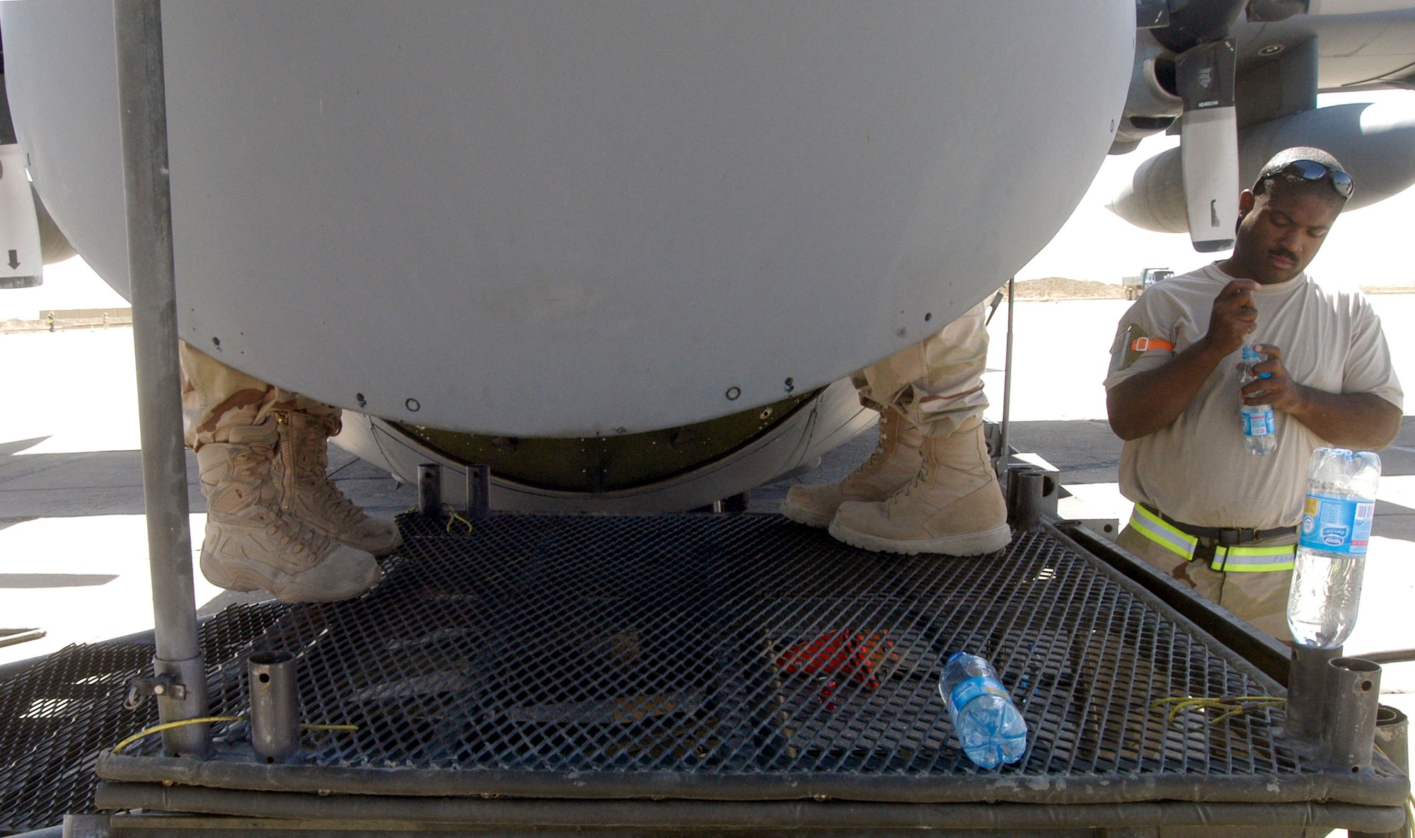 Staff Sgt. Alonzo Perry, right, takes a break for some water while two of his squadronmates continue installing safety wire on an APN-59 radar transmitter and receiver in the nose of a C-130 Hercules at Bagram Airfield, Afghanistan, Aug. 28.  Sergeant Perry is from the 166th Airlift Wing, Delaware Air National Guard.  He is deployed to the 455th Expeditionary Maintenance Group at Bagram in support of Operation Enduring Freedom.  He and three other communication and navigation system specialists replaced the radar antenna, then attached safety wire to the fasteners to prevent them from vibrating loose during flight.  The entire C-130 maintenance operation at Bagram is manned by members of the Air National Guard from all over the U.S.  (US Air Force photo/Maj. David Kurle)