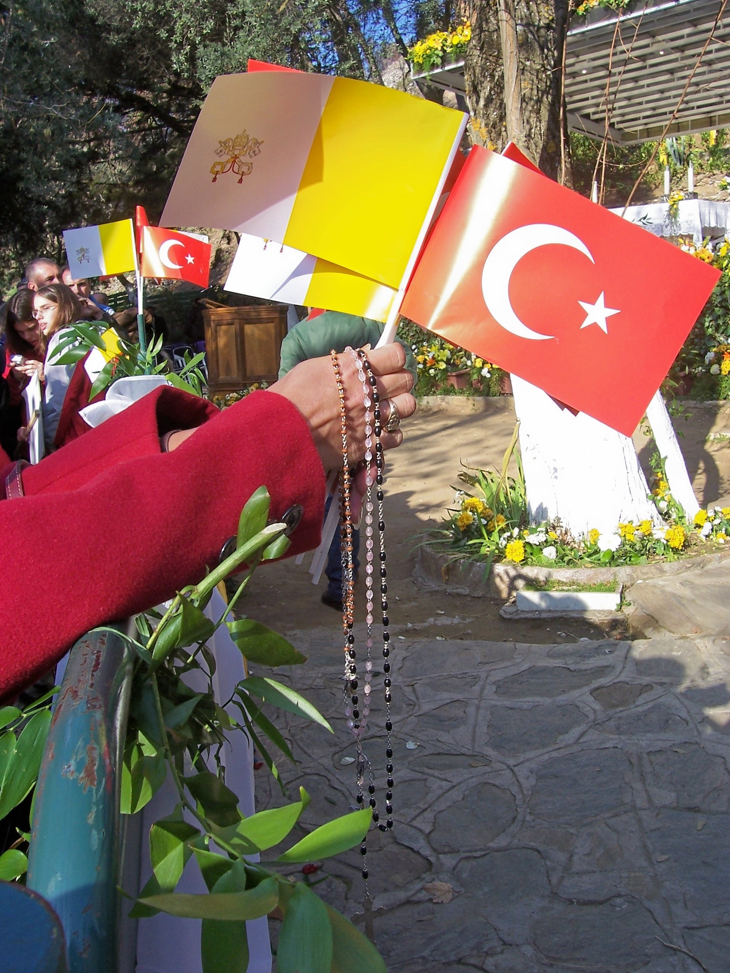 An attendee waits to celebrate mass with Pope Benedict XVI in Ephesus, Turkey, Nov. 29, holding the Catholic Flag, the Turkish flag and a number of rosaries.  (Courtesy photo)