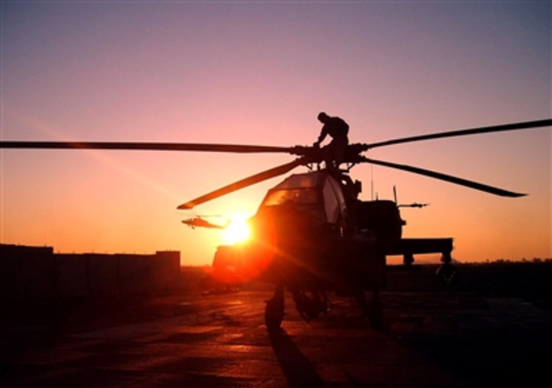 The sun rises behind an Apache crewmember with Company C, 4th Battalion, 227th Attack and Reconnaissance Battalion, who is preparing the helicopter for take off, Dec. 1, 2006. 