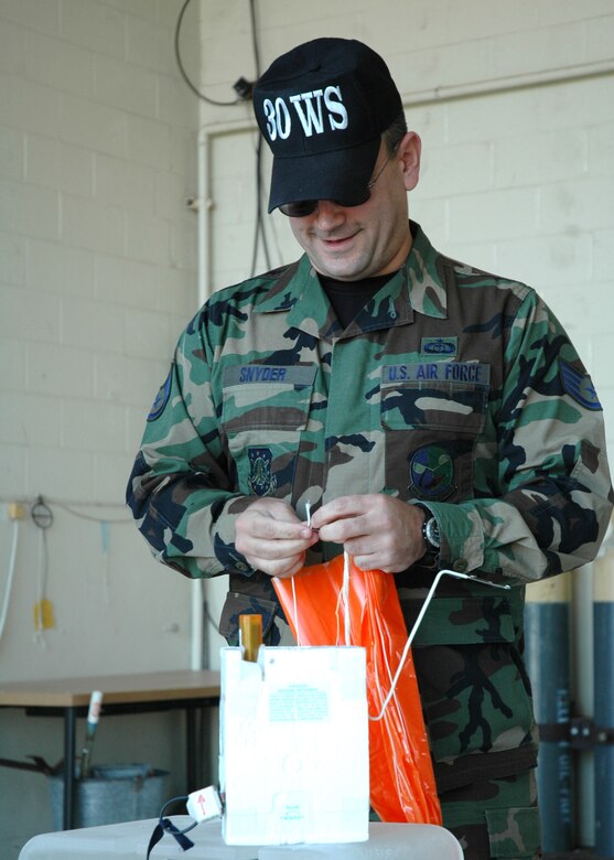 Staff Sgt. Brad Snyder, 30th Weather Squadron, attaches a parachute to the radiosonde which is then attached to a weather balloon at the balloon facility on Vandenberg.  The balloons travel to a height of more than 110,000 feet before exploding and sending the attached global positioning system gliding back to earth via the small parachute.  (U.S. Air Force photo by Staff Sgt. Raymond Hoy)