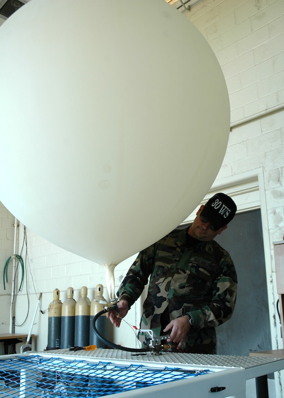 Staff Sgt. Brad Snyder, 30th Weather Squadron, fills a weather balloon with helium at the balloon facility on Vandenberg.  The balloons travel to a height of more than 110,000 feet before exploding and sending the attached global positioning system gliding back to earth via a small parachute.  (U.S. Air Force photo by Staff Sgt. Raymond Hoy)