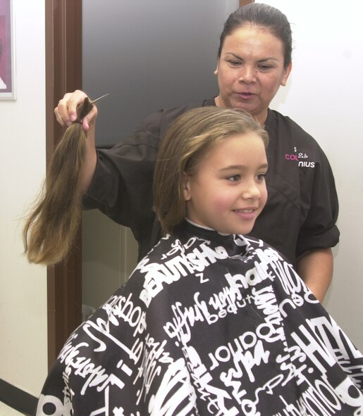 (Photo by Frank McIntyre) Antonia Herrera, Vance Air Force Base Barbershop beautician, holds the 11 inches of hair Catherine O’Bryan had cut to donate to the Locks of Love organization. Catherine is the daughter of Felicia and Capt. Timothy O’Bryan, 71st Security Forces Squadron. Emily Suttles, daughter of Debbie and Chief Master Sgt. Jim Suttles, 71st Flying Traiing Wing command chief, is currently growing her hair to donate to the organization as well.