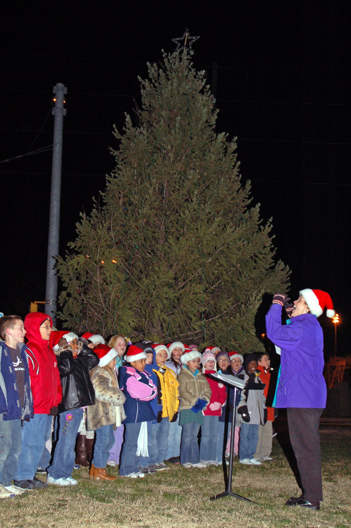 Diane Walls, Welch Elementary School music instructor, conducts the Welch Elementary Chorus, a choir comprised of 60 – 70 boys and girls from the base, during the Base Christmas Tree Lighting ceremony here Tuesday. (U.S. Air Force photo/Staff Sgt. James Wilkinson)