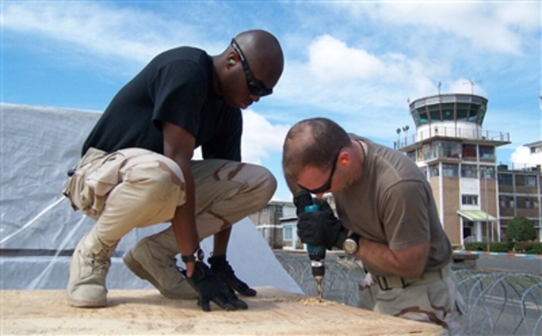 U.S. Air Force Tech. Sgt. Terreon Shirlee, deployed to the 386th Expeditionary Logistics Readiness Squadron, assists Capt. James King, commander of the Movement Control Team at the 386th ELRS, as they drill holes into plywood at Camp Lemonier, Djibouti, Dec. 10, 2006. The boards will serve as the base for pallets being air dropped into Eastern Kenya.