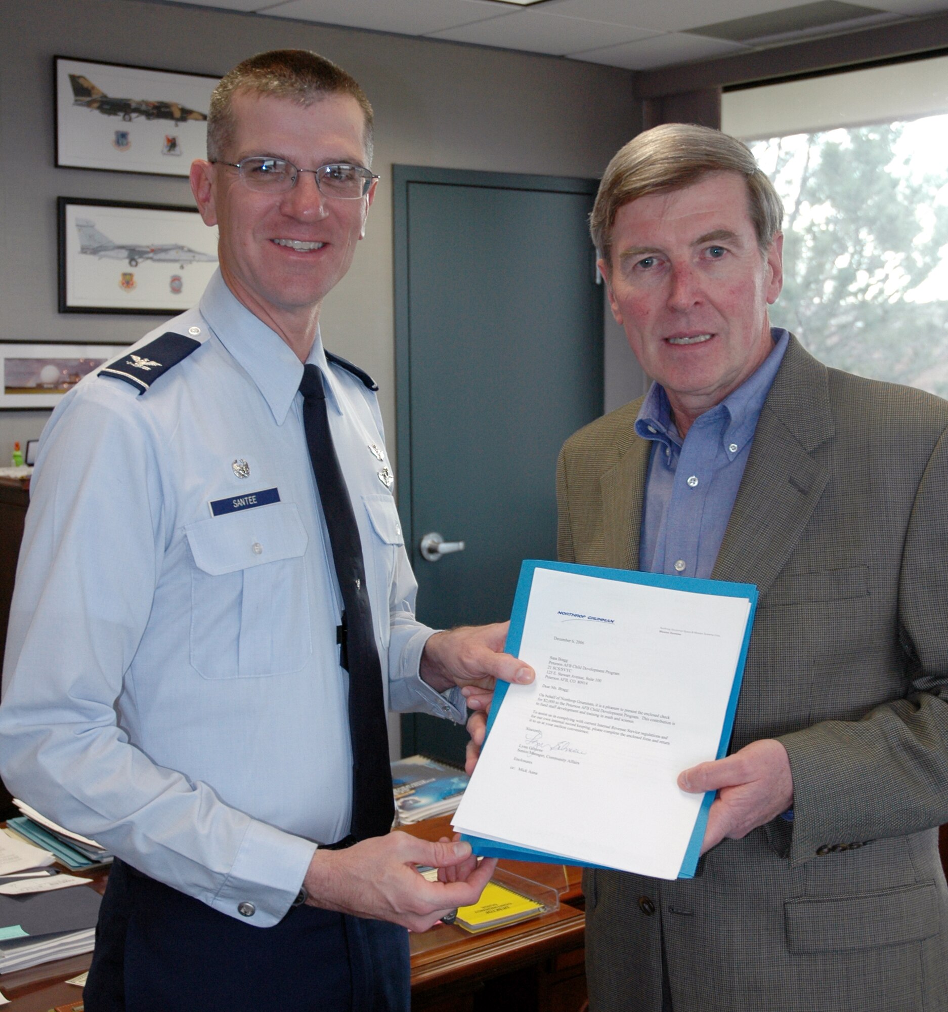 Tim McMahon of Northrop Grumman, presents a $2000 check to Col. Jay G. Santee, 21st Space Wing commander, Dec. 11 in the commander’s office for the benefit of the Peterson AFB Child Development Center. The money is for use at the CDC, Mr. McMahon said, to help take care of family members. Mr. McMahon is a retired major general and a former 21st Operations Group commander. 
(The photograph or event it depicts is in no way an express or implied endorsement by the Air Force or 21st Space Wing of Northrop Grumman )(U.S. Air Force photo by Steve Brady)