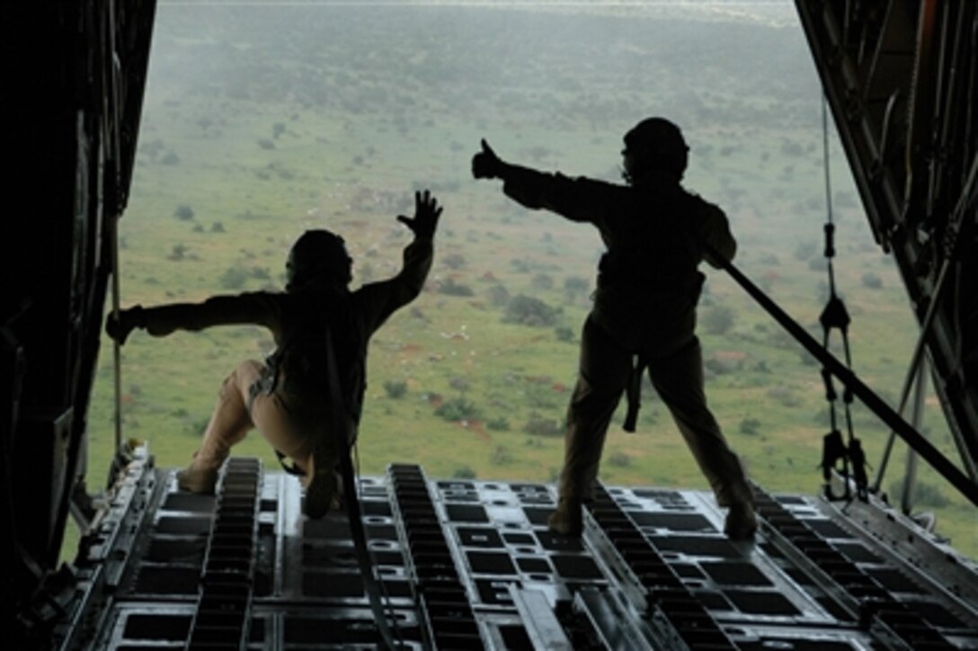 U.S. Air Force Senior Airman Chris Elder (left) and Staff Sgt. Patrick Delselva wave from their C-130 Hercules aircraft to people on the ground after a successful air drop of bundles of shelters and mosquito nets onto a field in Dadaab, Kenya, on Dec. 9, 2006. U.S. aircrews, assigned to Combined Joint Task Force - Horn of Africa, are air-dropping relief supplies and humanitarian aid for the approximately 160,000 stranded victims of recent flooding in rural areas of Kenya.  The airmen are C-130 Hercules aircraft loadmasters deployed from Dyess Air Force Base, Texas, to the 746th Expeditionary Airlift Squadron.  