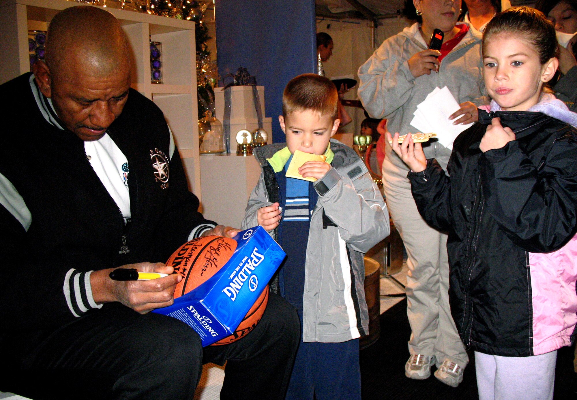 George Gervin signs a basketball for Carli and Blake Green during Operation Christmas Dec. 13 at the Texas National Guard Armory in San Antonio. Operation Christmas is an outreach program designed to show support to military families during the holiday season. Mr. Gervin is a retired San Antonio Spurs guard, and was named one of the NBA's top 50 players of all-time. (U.S. Air Force photo/Airman 1st Class Lana Mills) 